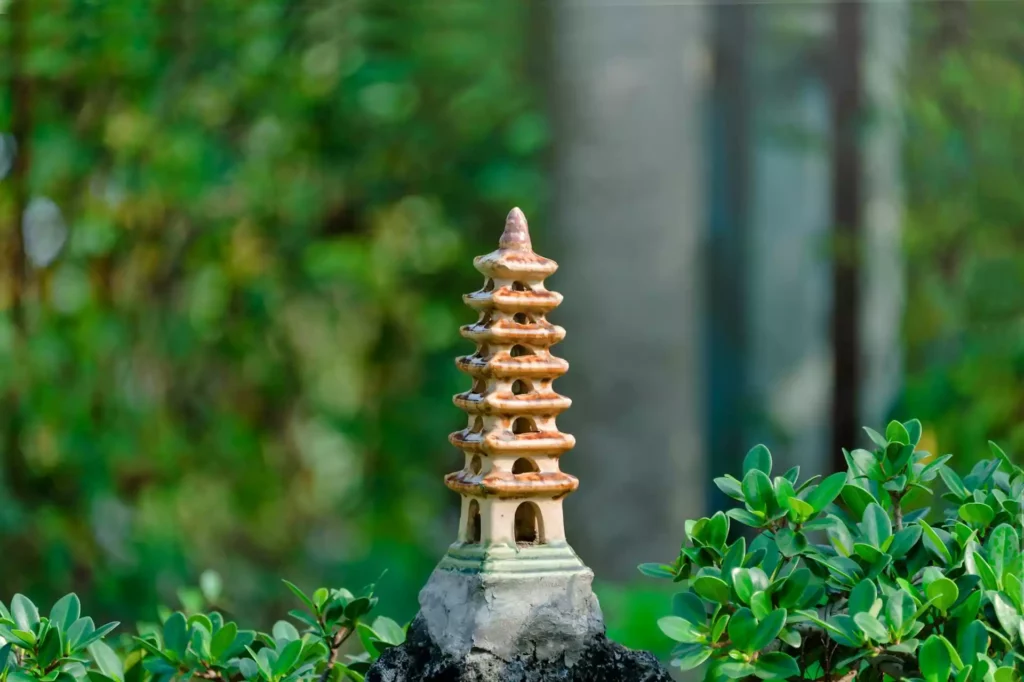 Une pagode miniature en céramique marron sur un fond flou de verdure et d'architecture.