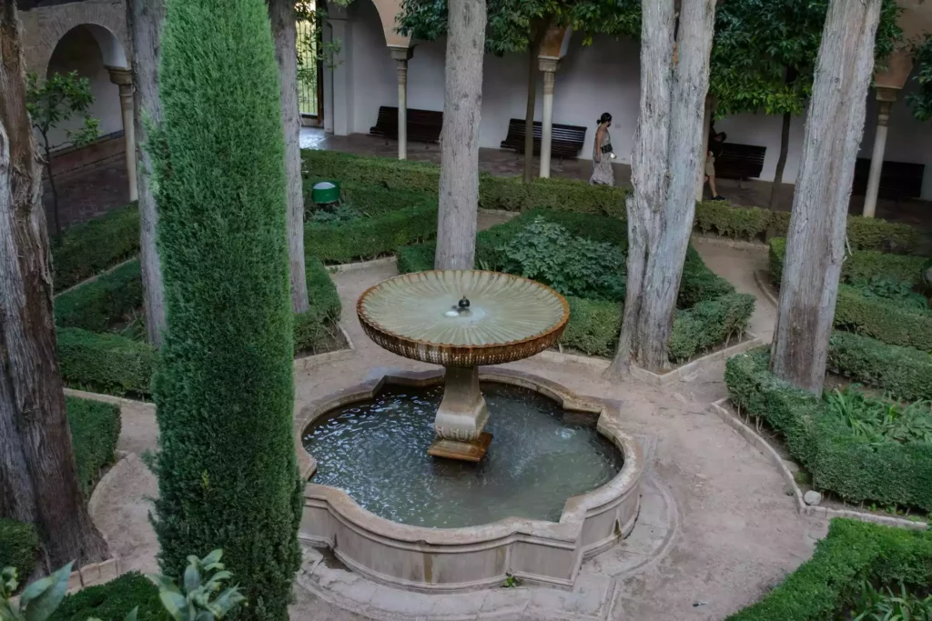 Vue surélevée d'une fontaine circulaire dans une cour, entourée de colonnes et de jardins taillés. 